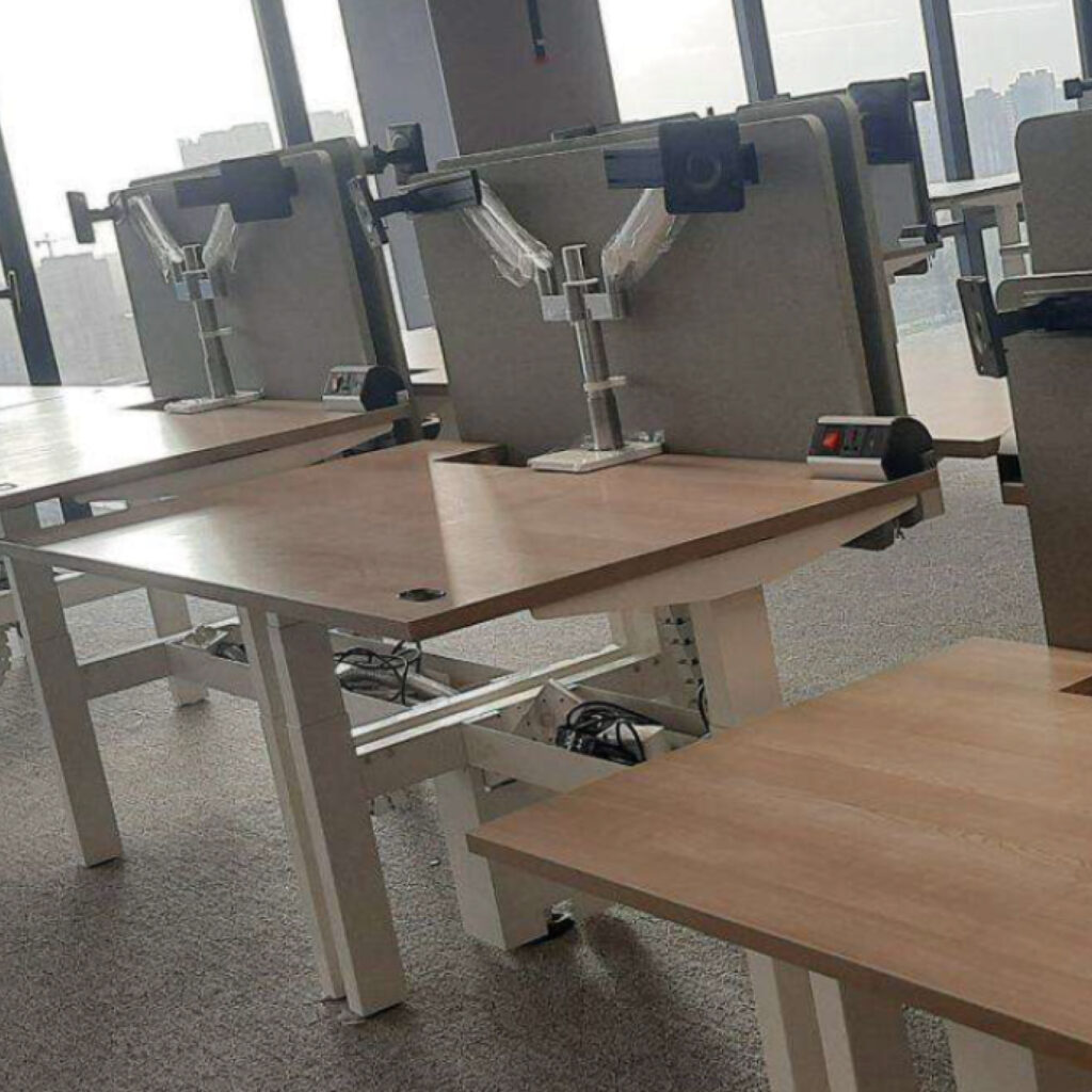 Empty office workspace with wooden desks and metal partitions in a bright, modern office.