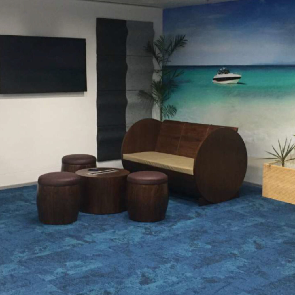 Lounge area with a blue ocean mural on the wall, dark brown round stools, a wooden coffee table, and a potted plant.