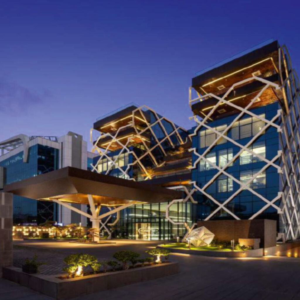 Nighttime view of a modern glass building with a white crisscross lattice facade and warm exterior lighting