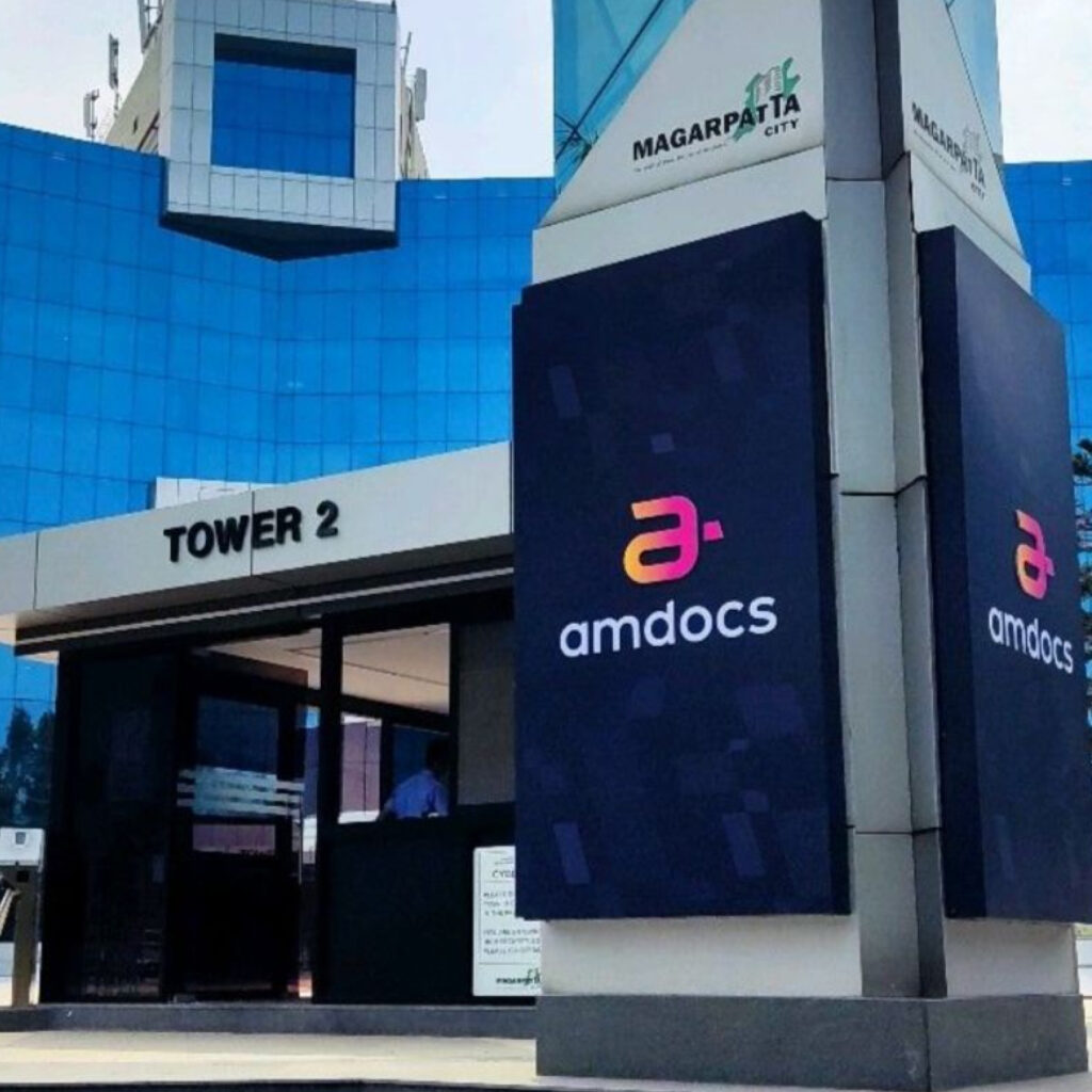 Blue glass office building with signage reading 'amdocs' on large black panels at the entrance area.