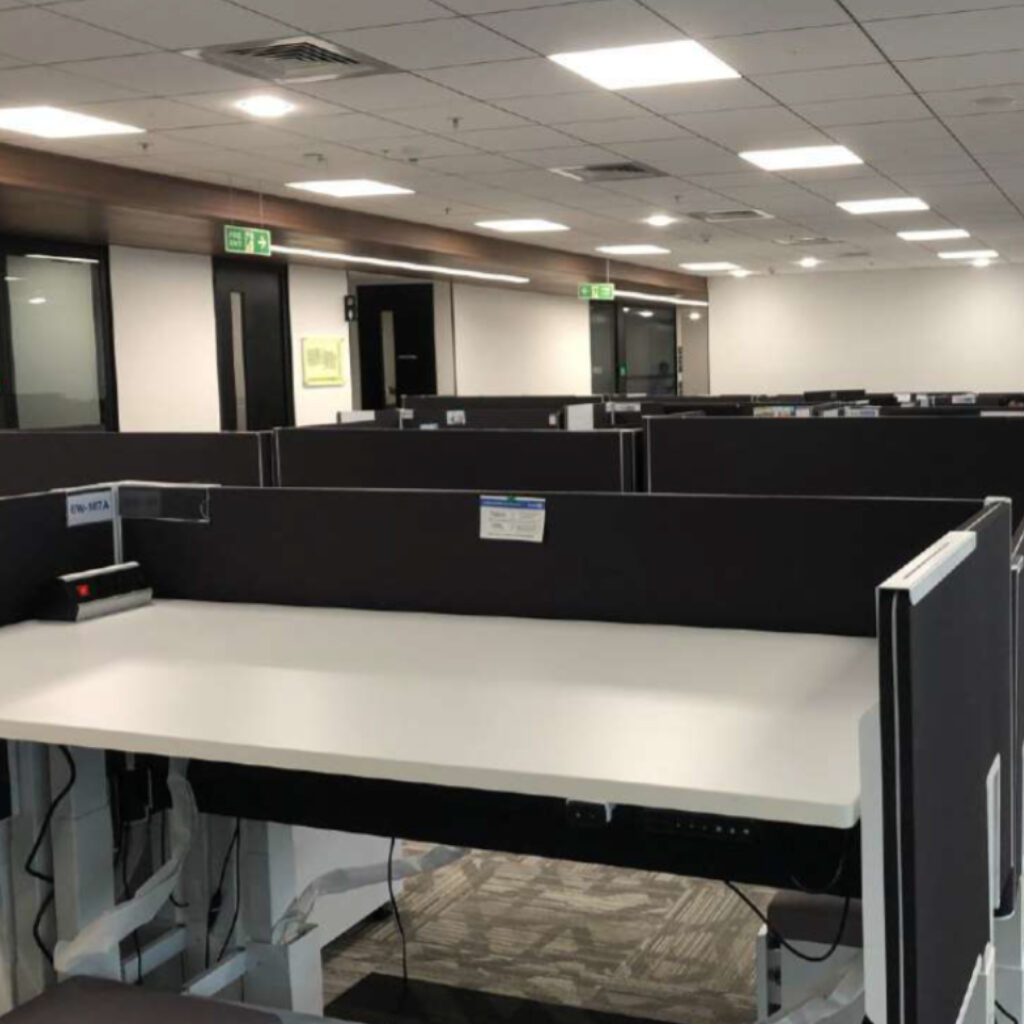 Open-plan office with rows of black partition cubicles and ceiling fluorescent lights.