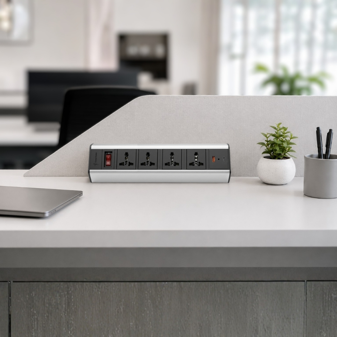 Power strip with six outlets and a USB port on a tidy desk, divider behind, plant to the right.
