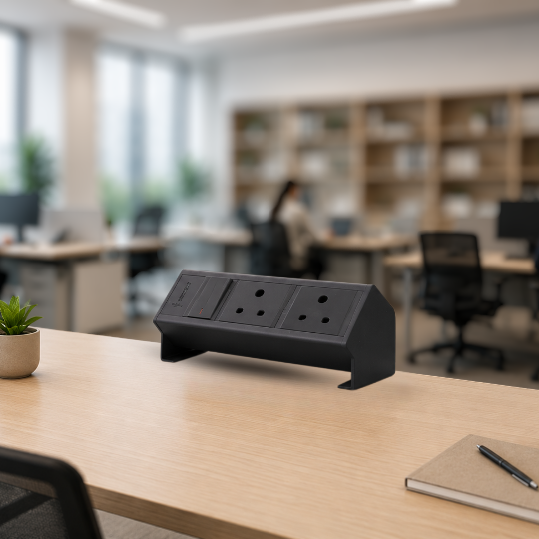 table connect raised india - Connect System - Connect System Black multi-socket desk power strip on a wooden table in a bright open-office setting, with shelves in the background.